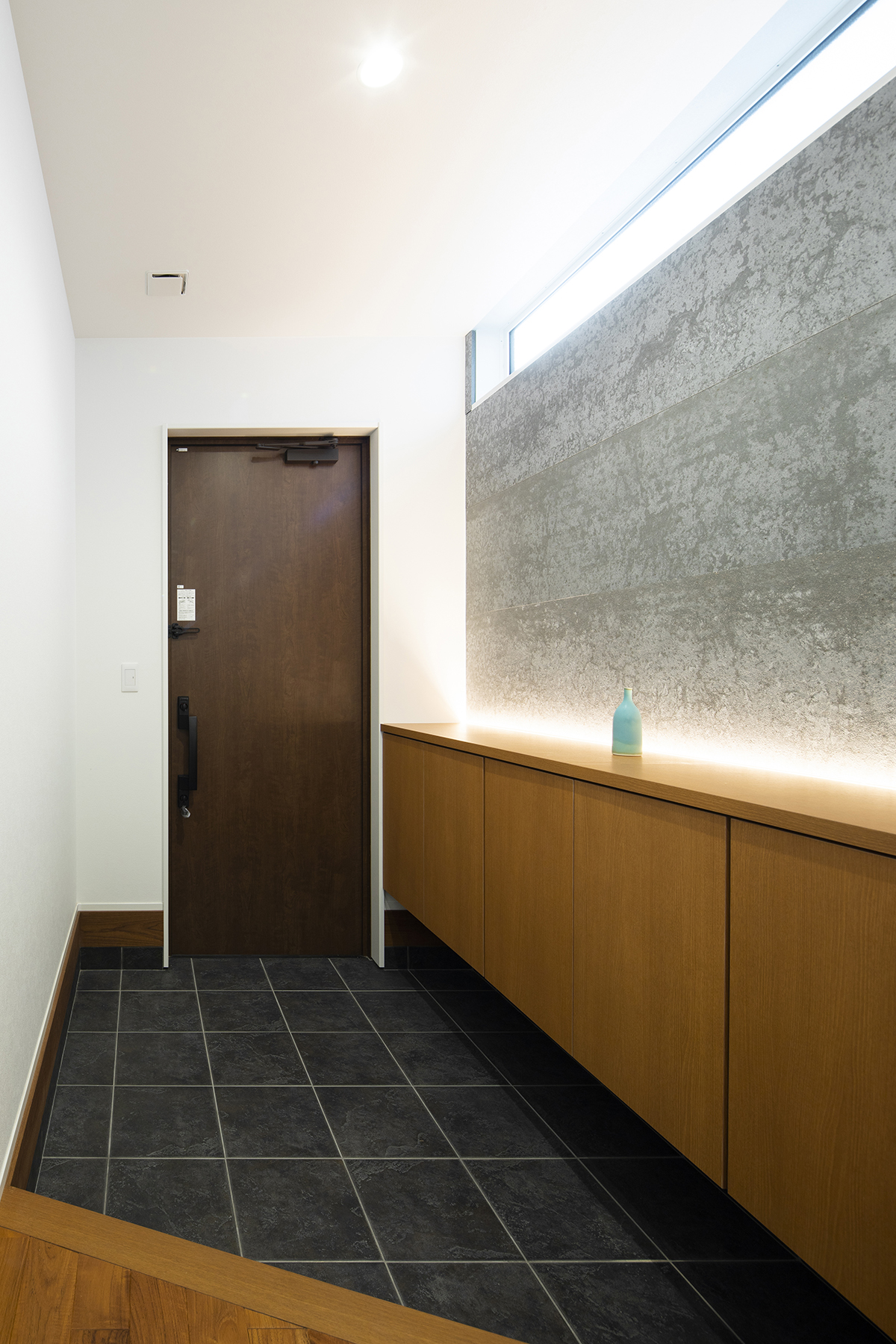 玄関の壁には、使用済みのコーヒー豆を原料にした建材を使用。味わい豊かな風合いを間接照明でライトアップ。