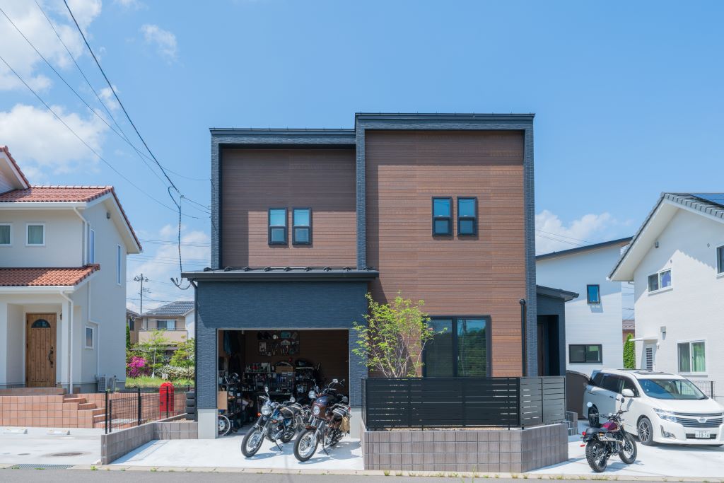 いくつかの箱を組み合わせたかのようなバイクガレージのある住まい。ネイビーとウッド調の外壁や、直線的なデザインがスタイリッシュに映えます。